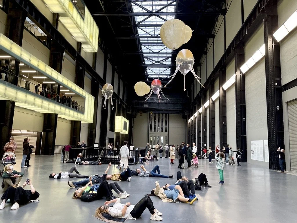 Aerobes drifting through the Turbine Hall's skylight-lit atrium as visitors below lie on the floor and look up