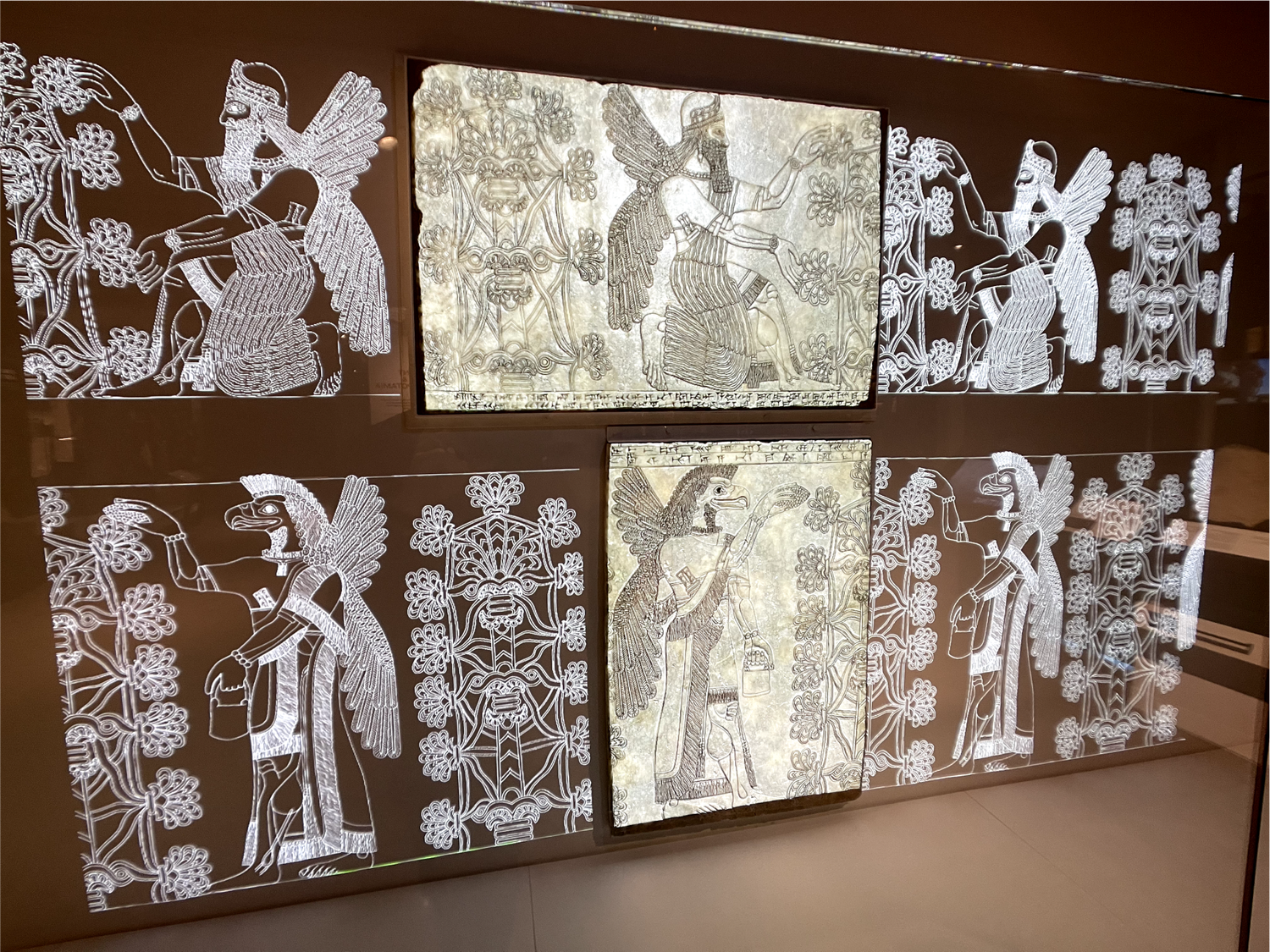 Backlit glass panels tracing Assyrian relief carvings around two authentic stone relief fragments in a gallery case
