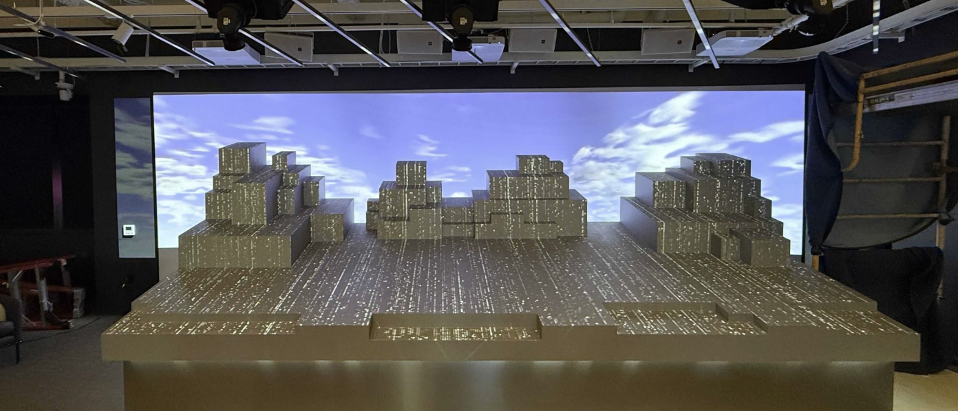 The architectural model mid-installation, showing a data-textured cityscape rendering against a sky backdrop on the projection screen