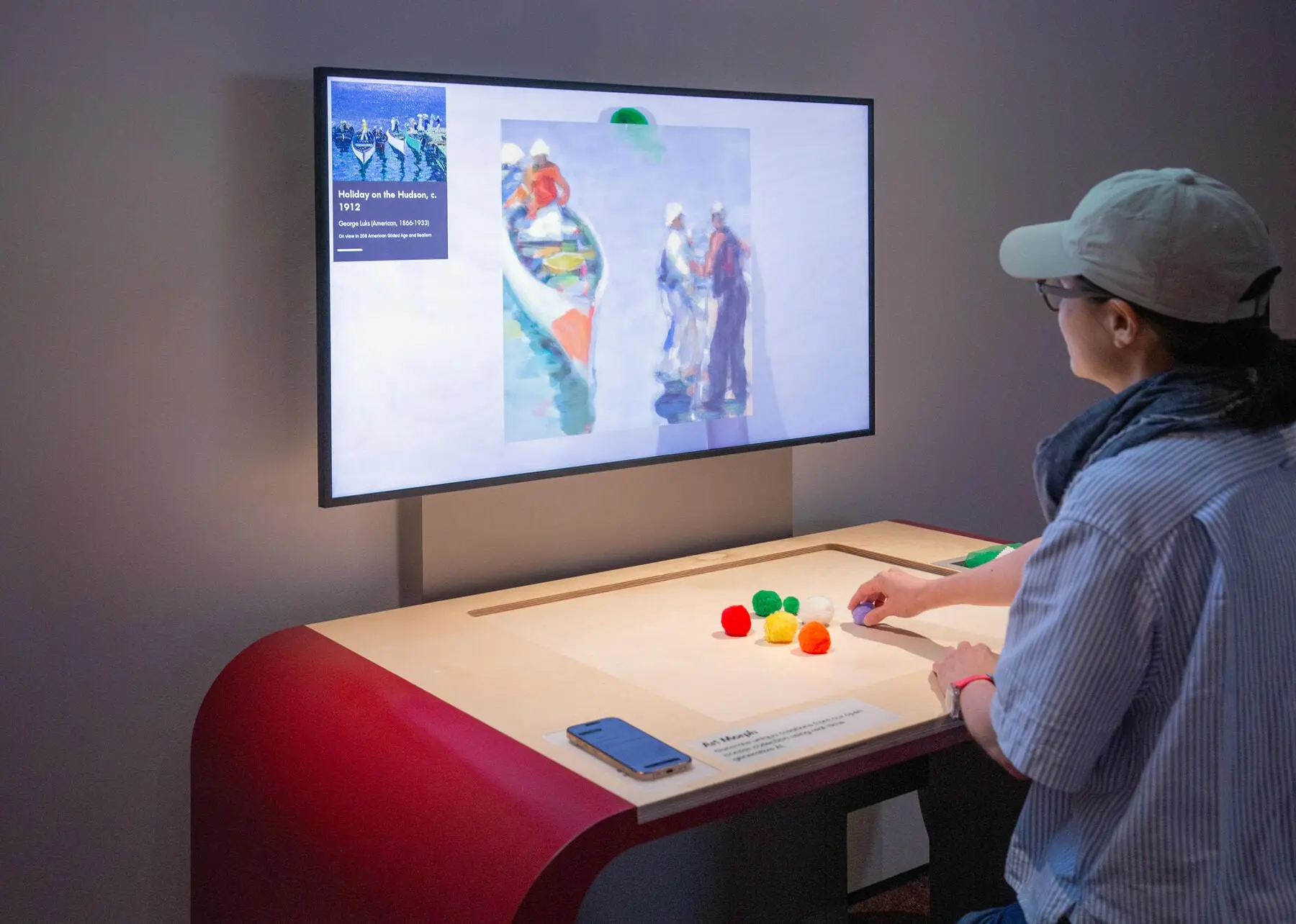 A visitor arranging tangible objects at the Art Morph interactive, recomposing a collection painting on the screen above from live collection data